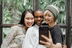 Cheerful young ladies hugging and taking selfie in modern cafe